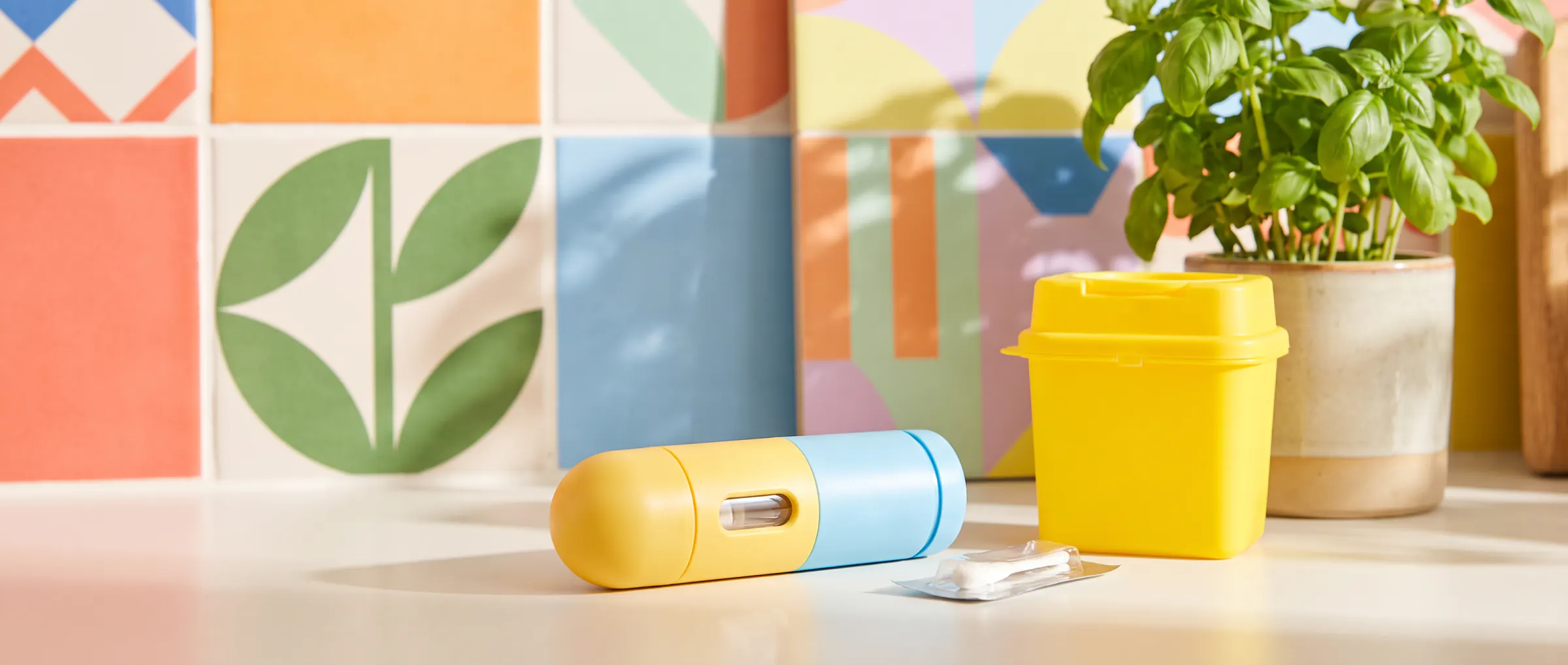 An injection pen, a swab and a small sharps bin on a bright kitchen counter